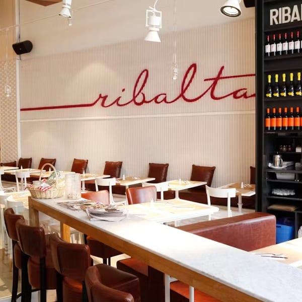 Ribalta restaurant interior with a long bar, dining tables, and a wine display.