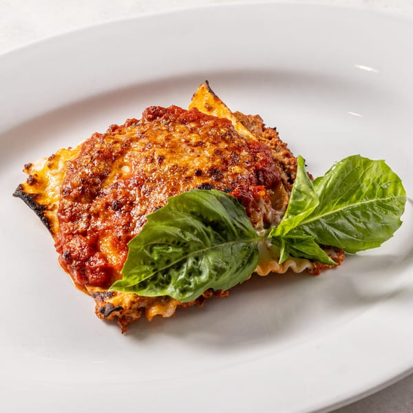 A serving of Ribalta's lasagna, topped with rich red sauce, melted cheese, and fresh basil leaves.