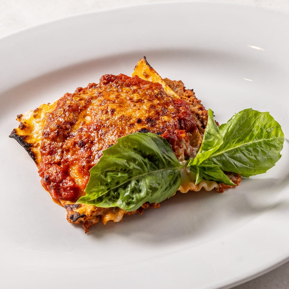 A serving of Ribalta's lasagna, topped with rich red sauce, melted cheese, and fresh basil leaves.