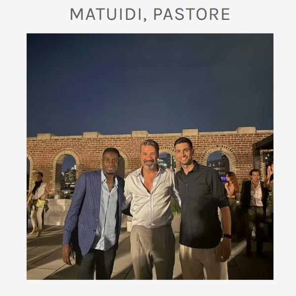 Three men smiling at the camera on a rooftop patio at night, with a brick wall behind them.