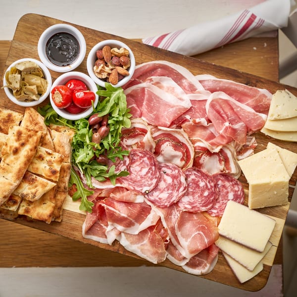 An Italian charcuterie board with various meats, cheeses, flatbread, olives, nuts, and sauces.
