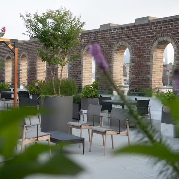 Rooftop patio with modern chairs, tables, potted plants, and brick arches in the background.