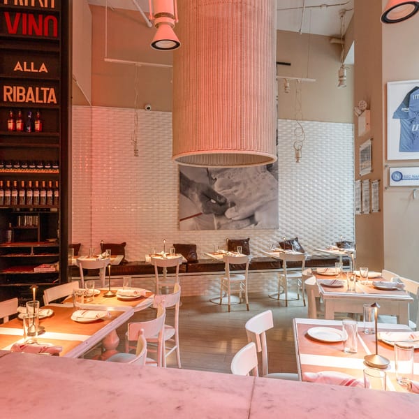 Ribalta's dining room with set tables, white chairs, a large woven light fixture, and a wine display.