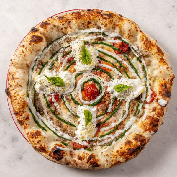 A Ribalta pizza with sausage, cherry tomatoes, pesto, burrata, and basil on a red plate.