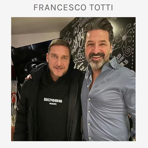 Two men, Francesco Totti and another, smiling at the camera in an Italian restaurant.