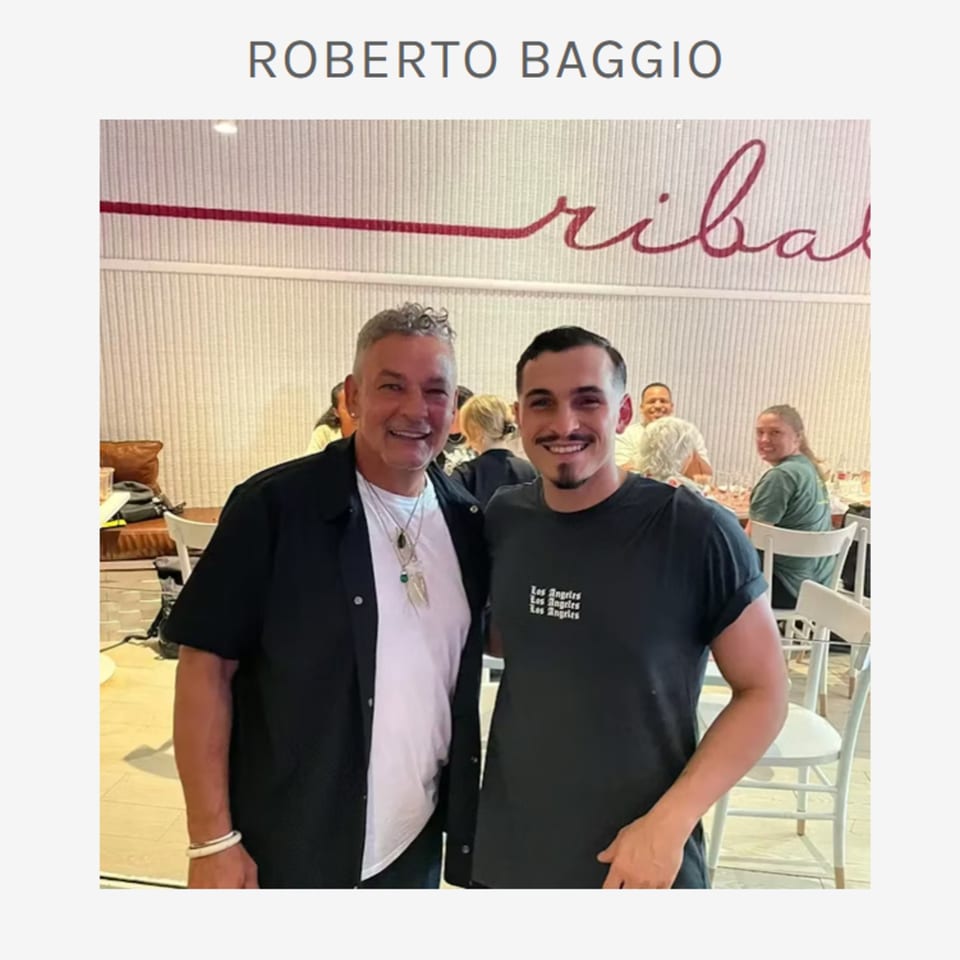 Two men smiling at the camera inside Ribalta, an Italian restaurant, with other diners in the background.