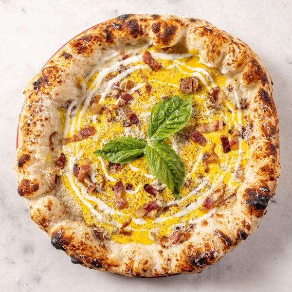 Ribalta's carbonara pizza with a creamy yellow sauce, crispy bacon, black pepper, and basil.