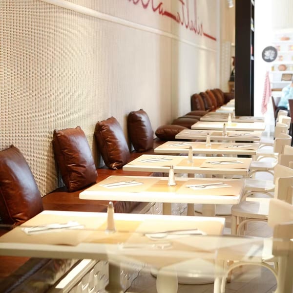 Long row of set tables with white chairs and brown leather bench seating at Ribalta.