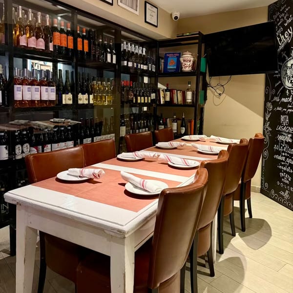 Long dining table set with plates and napkins, surrounded by brown leather chairs and wine shelves.