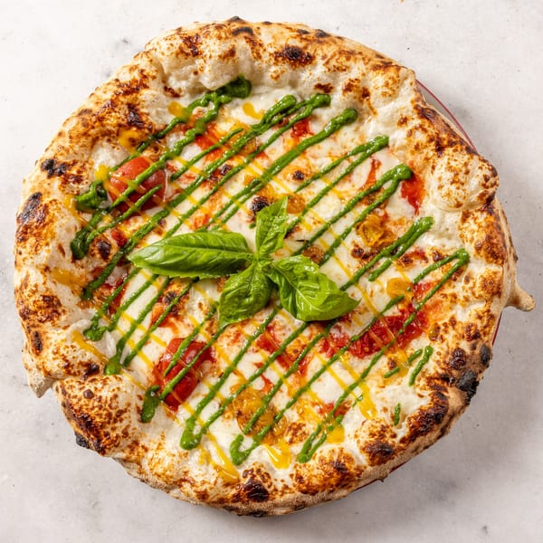 Neapolitan pizza with fresh mozzarella, red and yellow tomatoes, pesto, and a basil garnish.