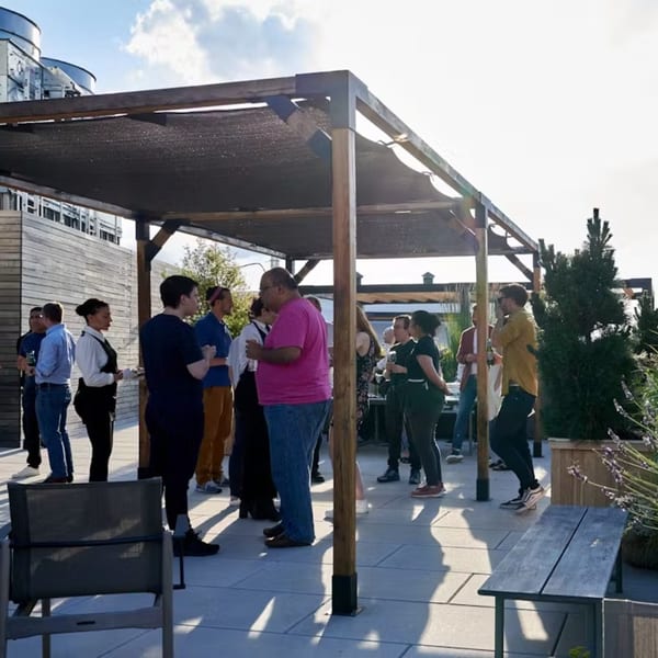 Guests mingle on a sunny rooftop patio under a shaded pergola at Ribalta.
